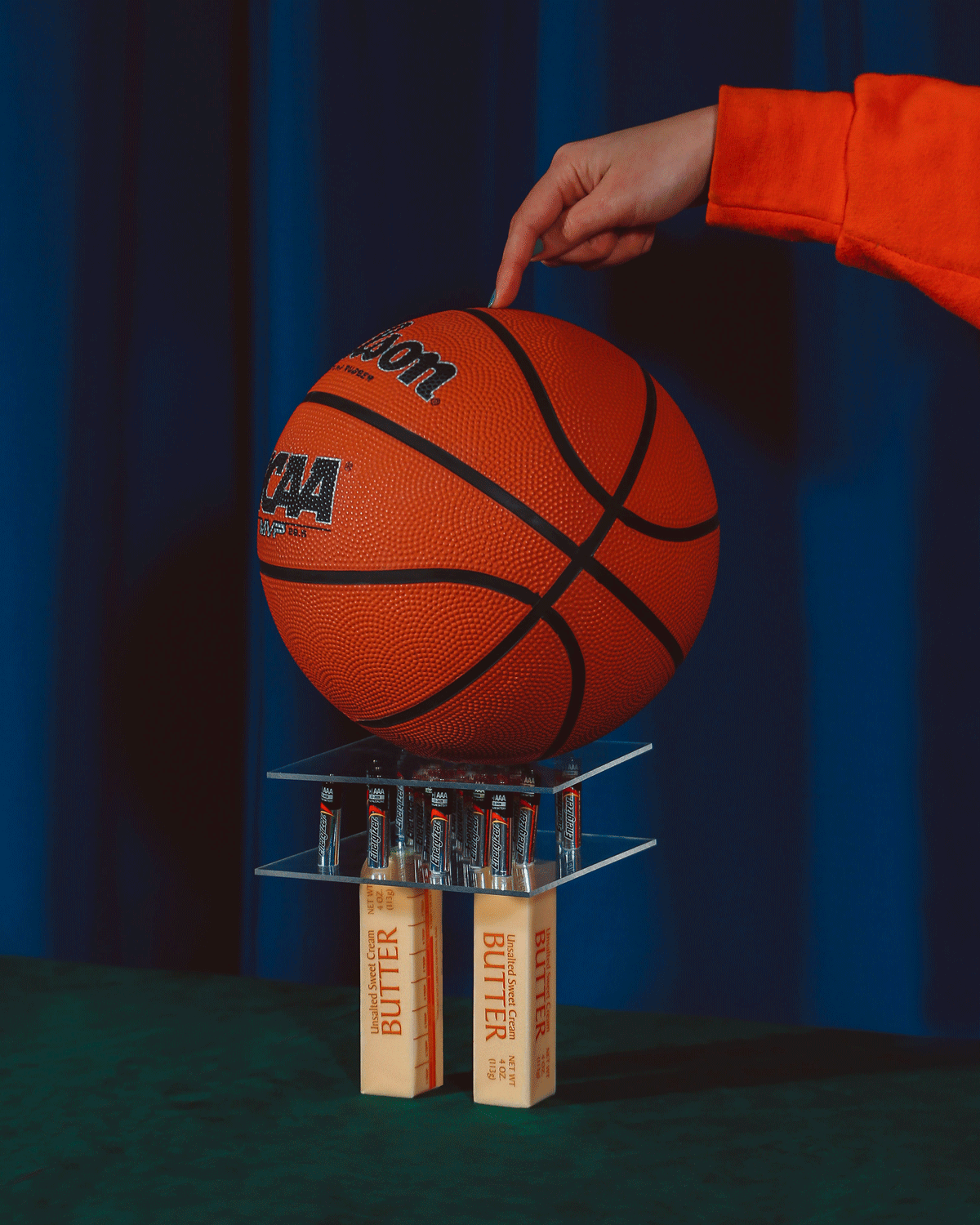 Photo conceptuelle d'une main maintenant en équilibre un ballon de basket sur plaques de verres. Le tout en équilibre sur des emballages rectangulaires de beurre 