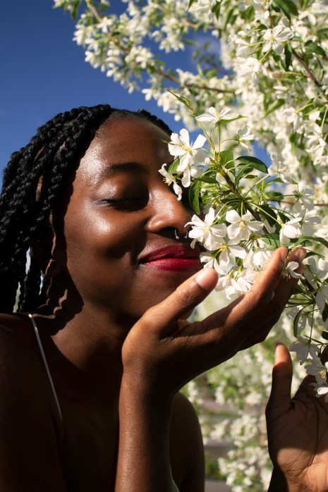 Femme de couleur noire sentant des fleurs blanches