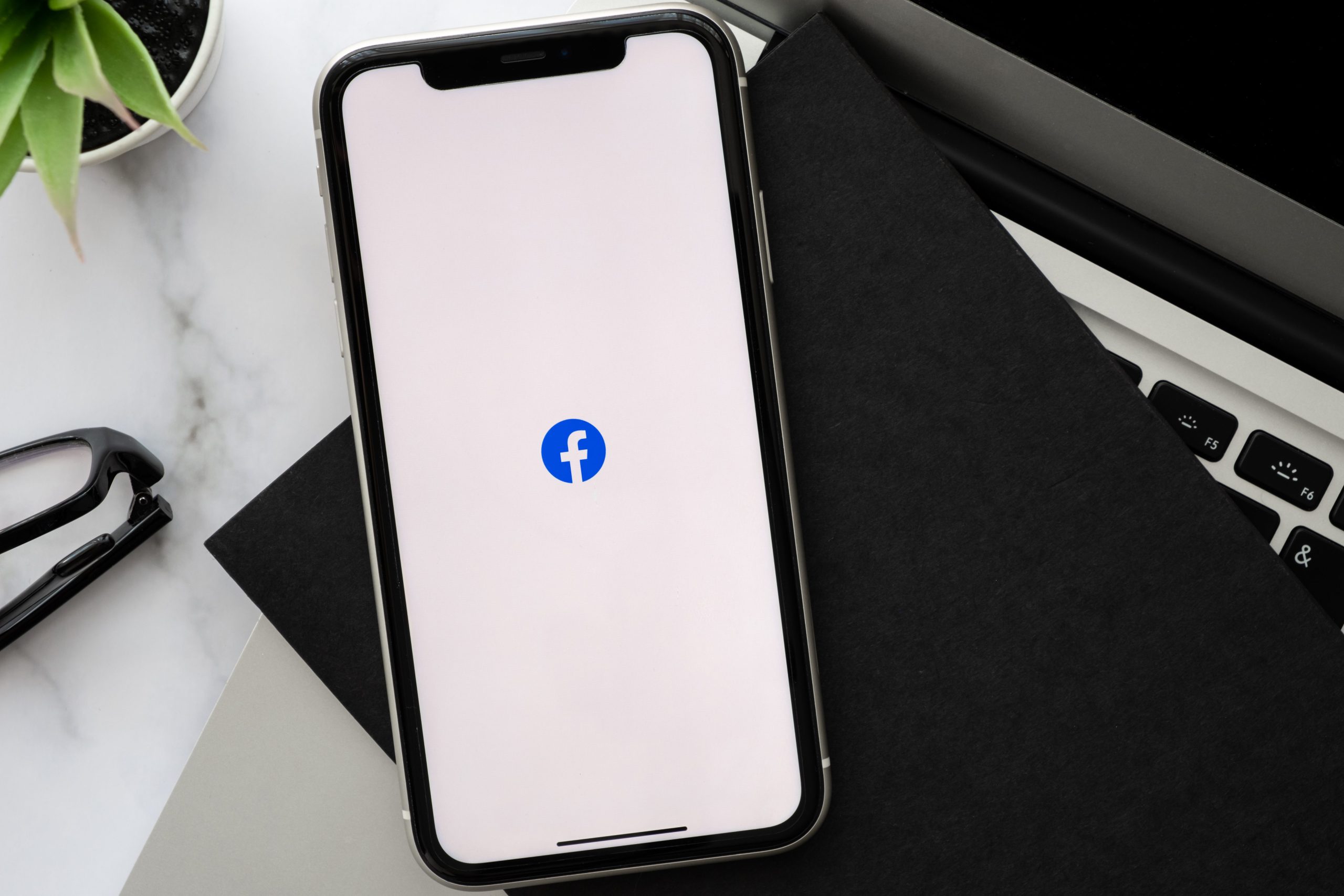 Smartphone affichant le logo de Facebook. Ce dernier est posé sur un ordinateur portable