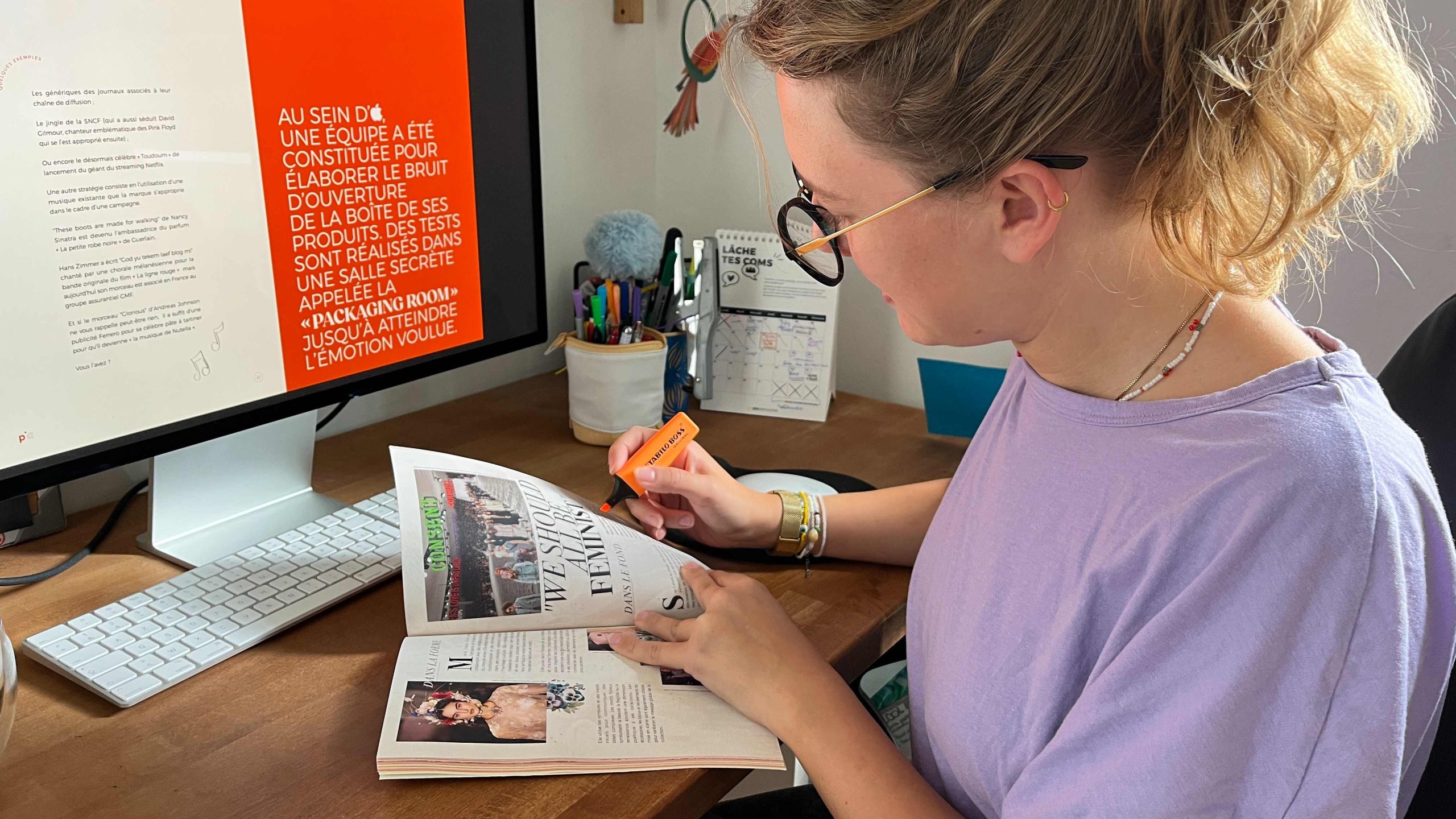 La directrice artistique de Pix Associates en train d’apporter des corrections sur le livre SENS après des tests d’impression. Vêtue d’un t-shirt mauve, d’une paire de lunettes noires et dorées, elle surligne de la main droite des textes à l’aide d’un surligneur orange.