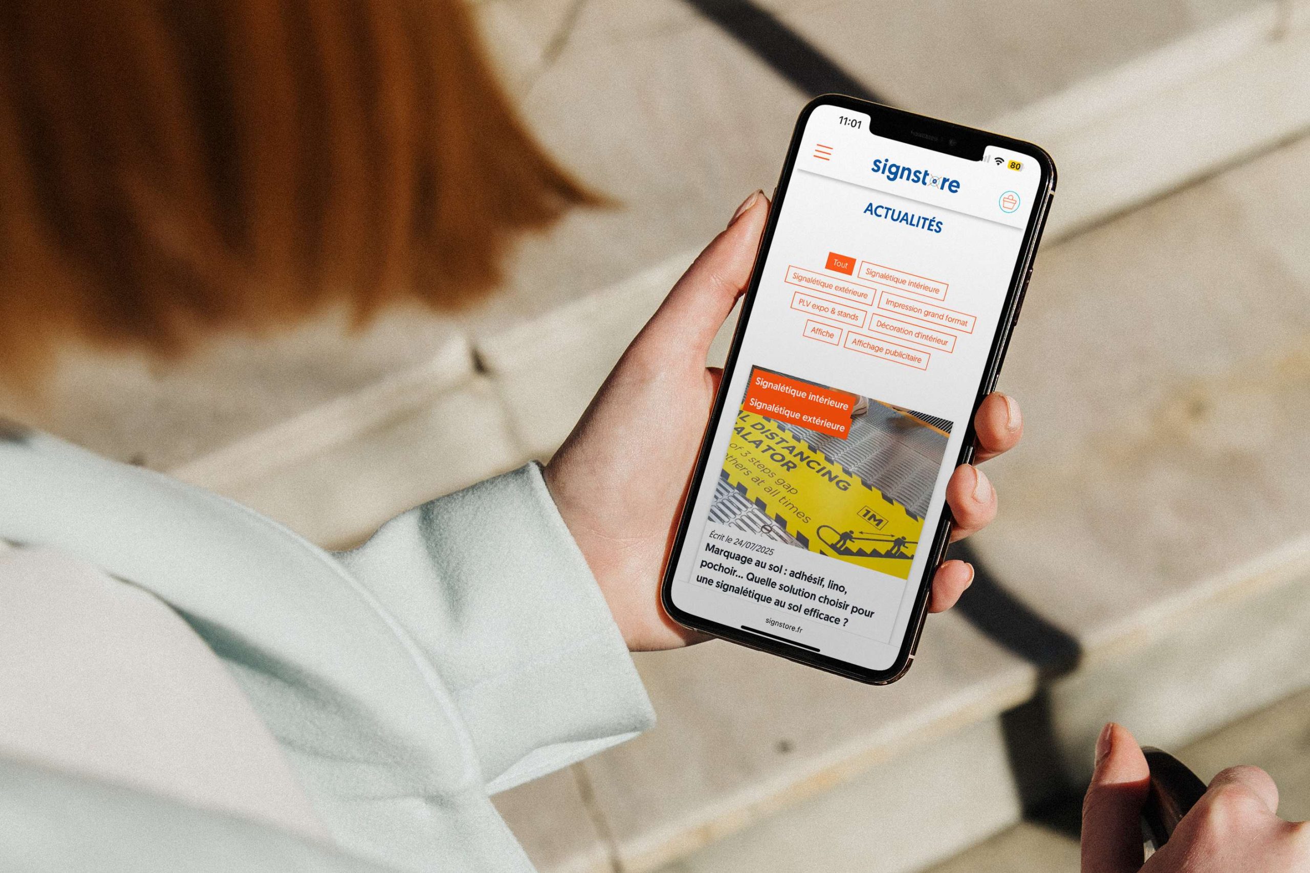 Femme consultant le site internet Signstore depuis la rubrique actualités sur la signalétique intérieure et extérieure via un smartphone.